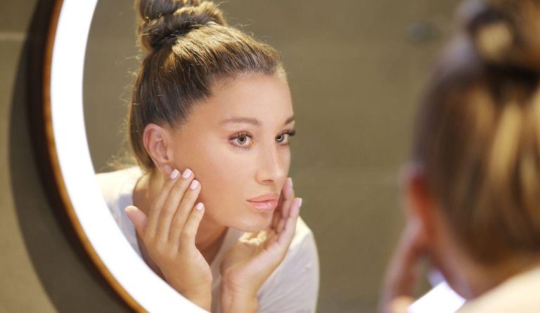 Donna davanti allo specchio con luce ad anello mentre controlla la pelle del viso durante una routine anti age